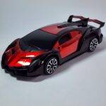 Black and metallic red RC Supercar model with large rear spoiler next to its black remote controller. Khilone for kids